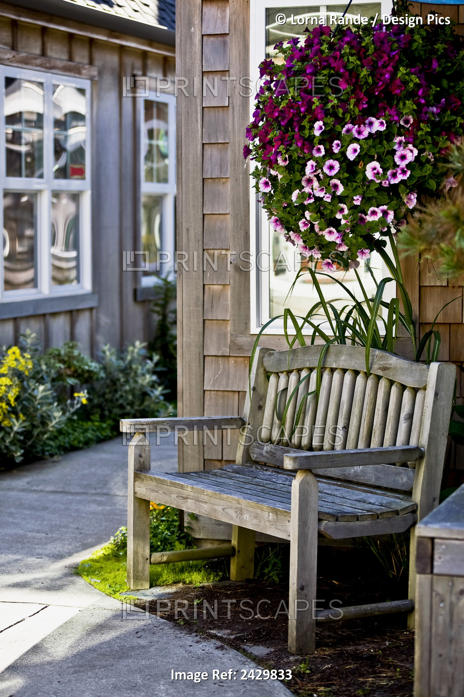 A Wood Bench And Hanging Flower Basket Along A Path Outside Retail Shops; ...