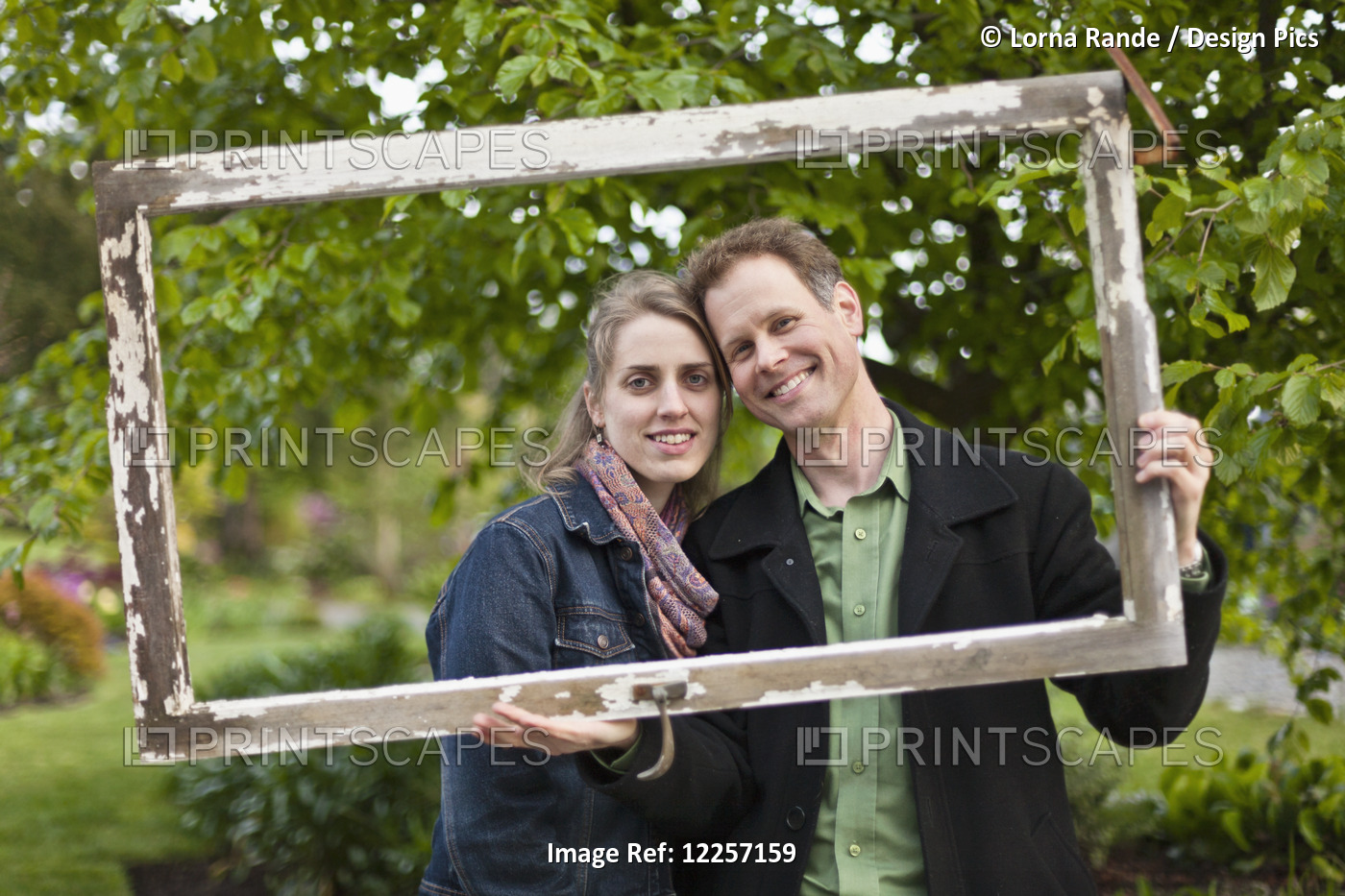 A Couple Posing For A Portrait Holding A Wooden Frame Around Their Faces; ...