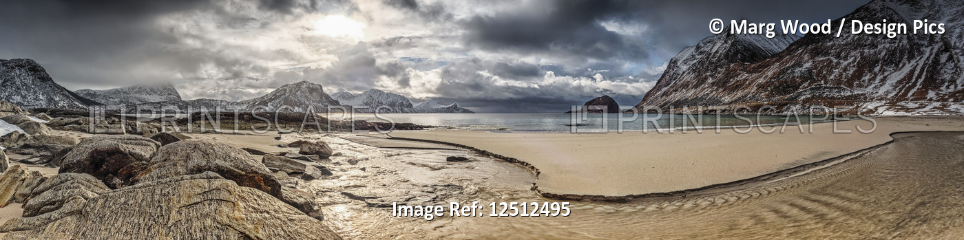 A landscape with rugged mountains and sand along the coastline under a cloudy ...