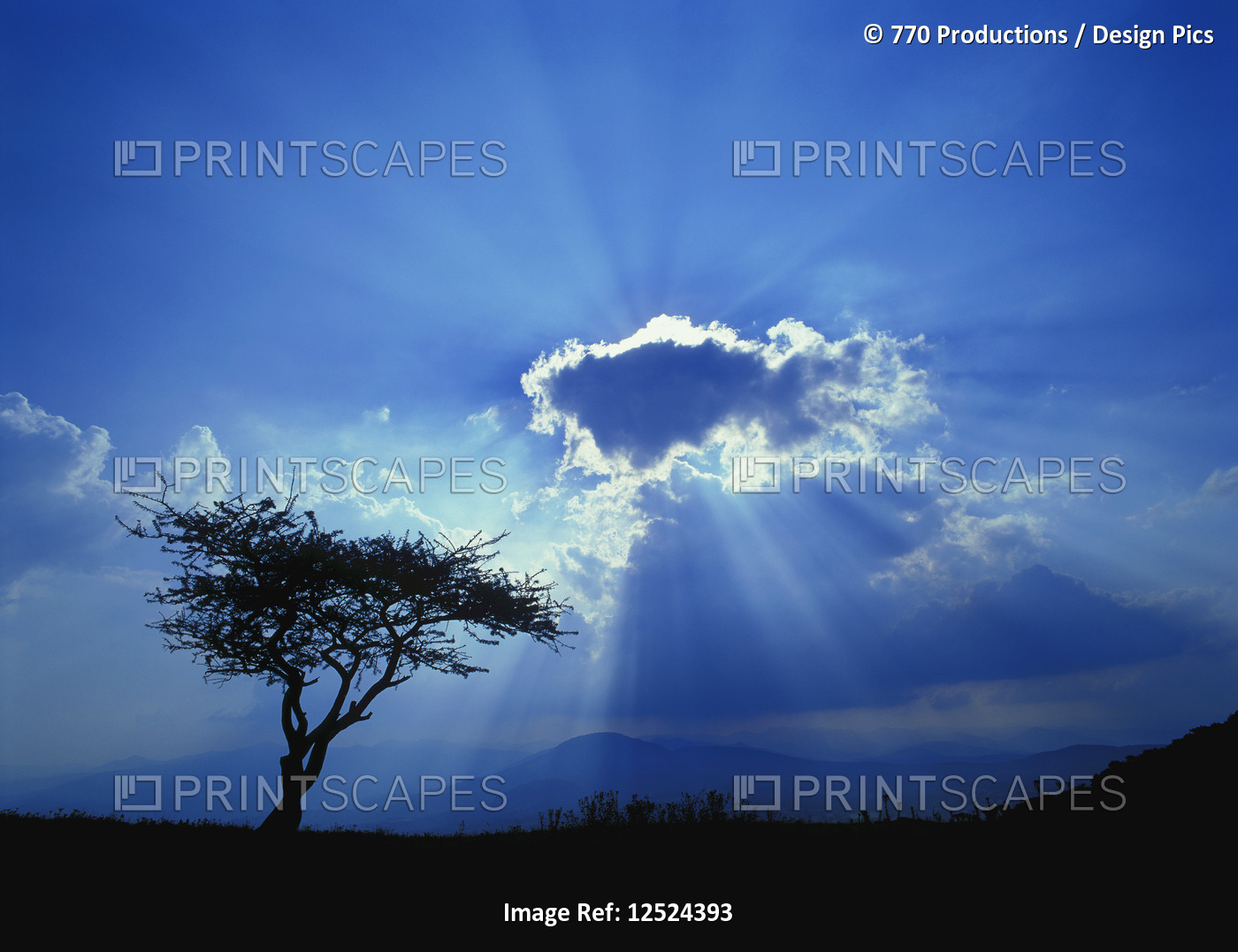 Sun rays burst around a glowing cloud to a silhouetted landscape below, near ...