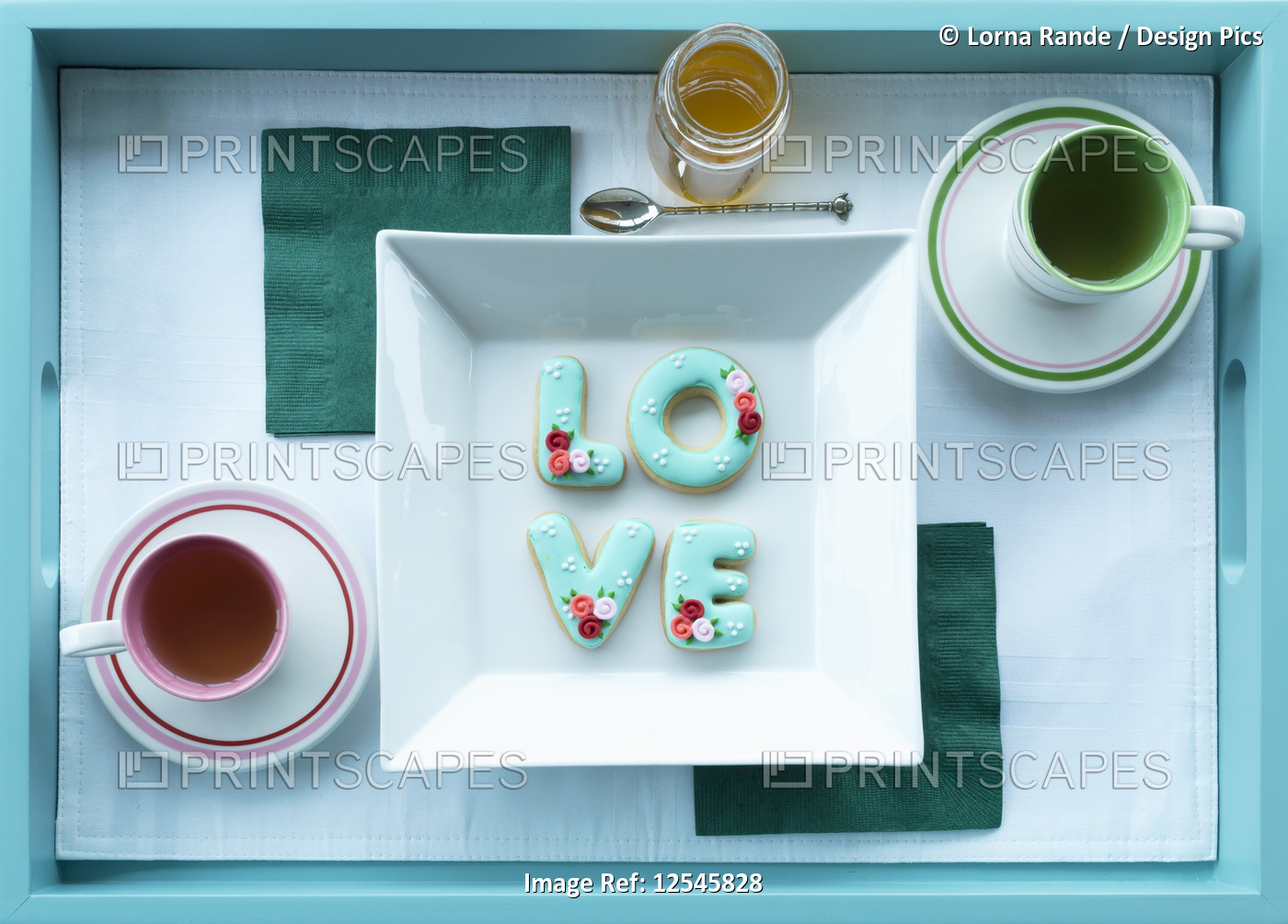 Tea in cups with saucers and cookies spelling out love on a tray