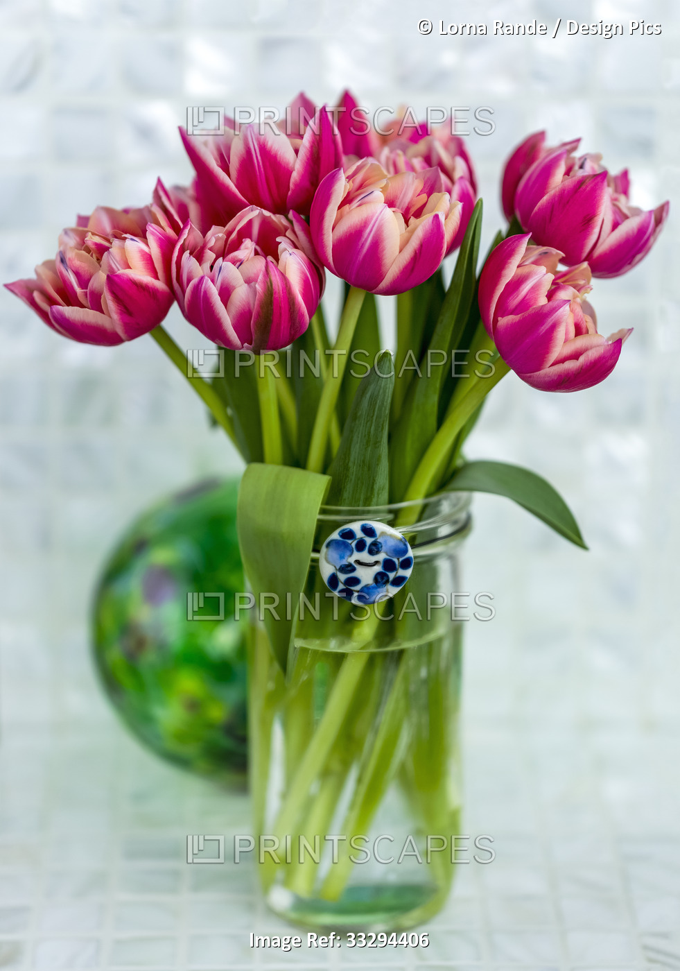 Pink tulips arranged in a glass vase with blue and white ceramic button on the ...