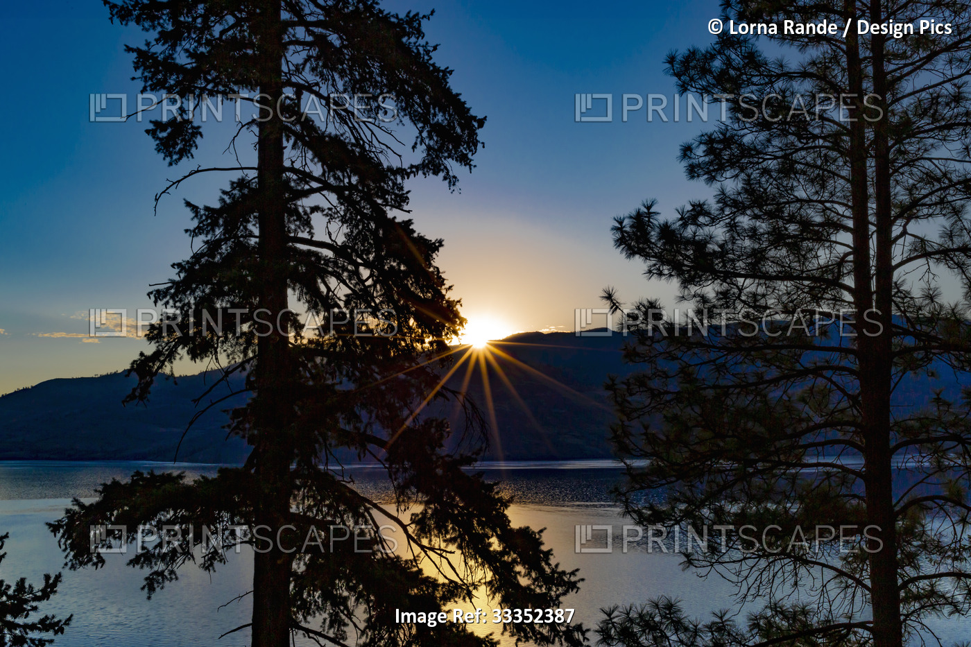Sunburst over the hills at sunset and Okanagan Lake framed by silhouetted ...