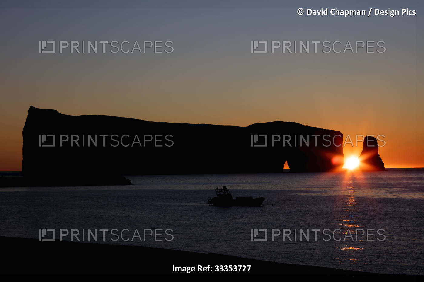 Perce Rock at sunset with the bright sun sinking down over the horizon; Quebec, ...