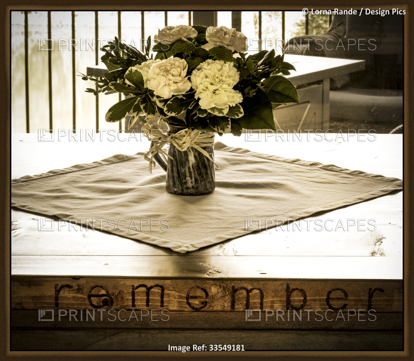 Framed artwork in sepia tone showing a flower arrangement in a home on a wooden ...
