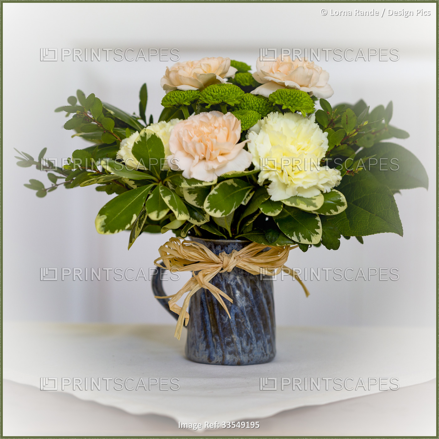 Flower arrangement of carnations and greenery in a jug vase tied with raffia on ...