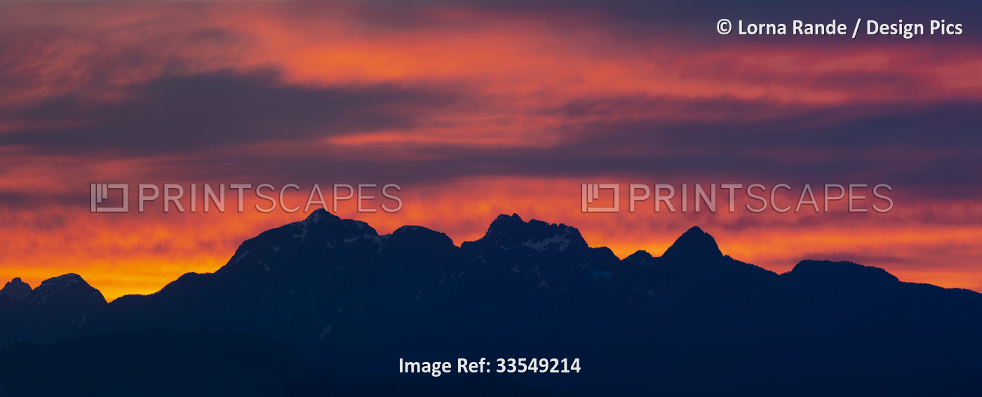 Vibrant coloured sunset over the silhouetted mountains; Surrey, British ...