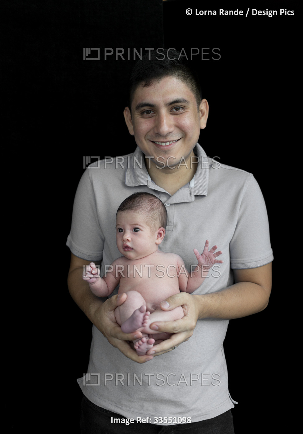 Portrait of father holding his newborn baby girl against a black background; ...