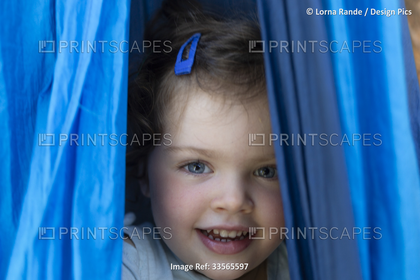 Close-up portrait of a preschooler girl with blue eyes and rosy cheeks peeking ...