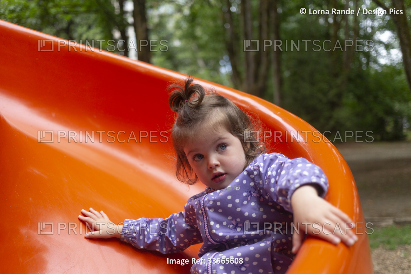 Preschool girl at a playground going down a red slide; North Vancouver, British ...