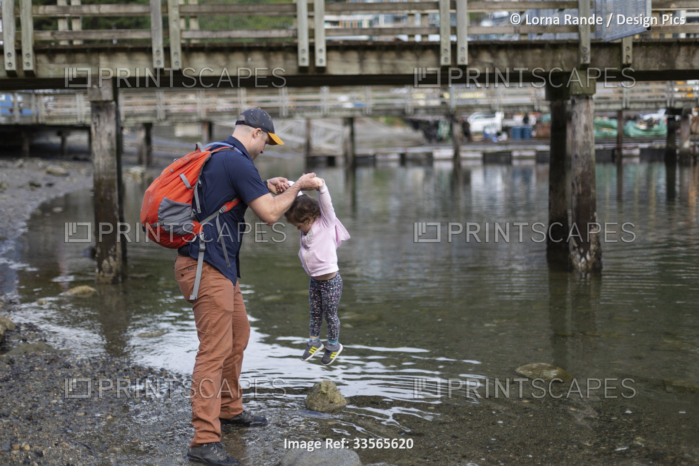 Father and young daughter being playful at the water's edge of a beach at the ...