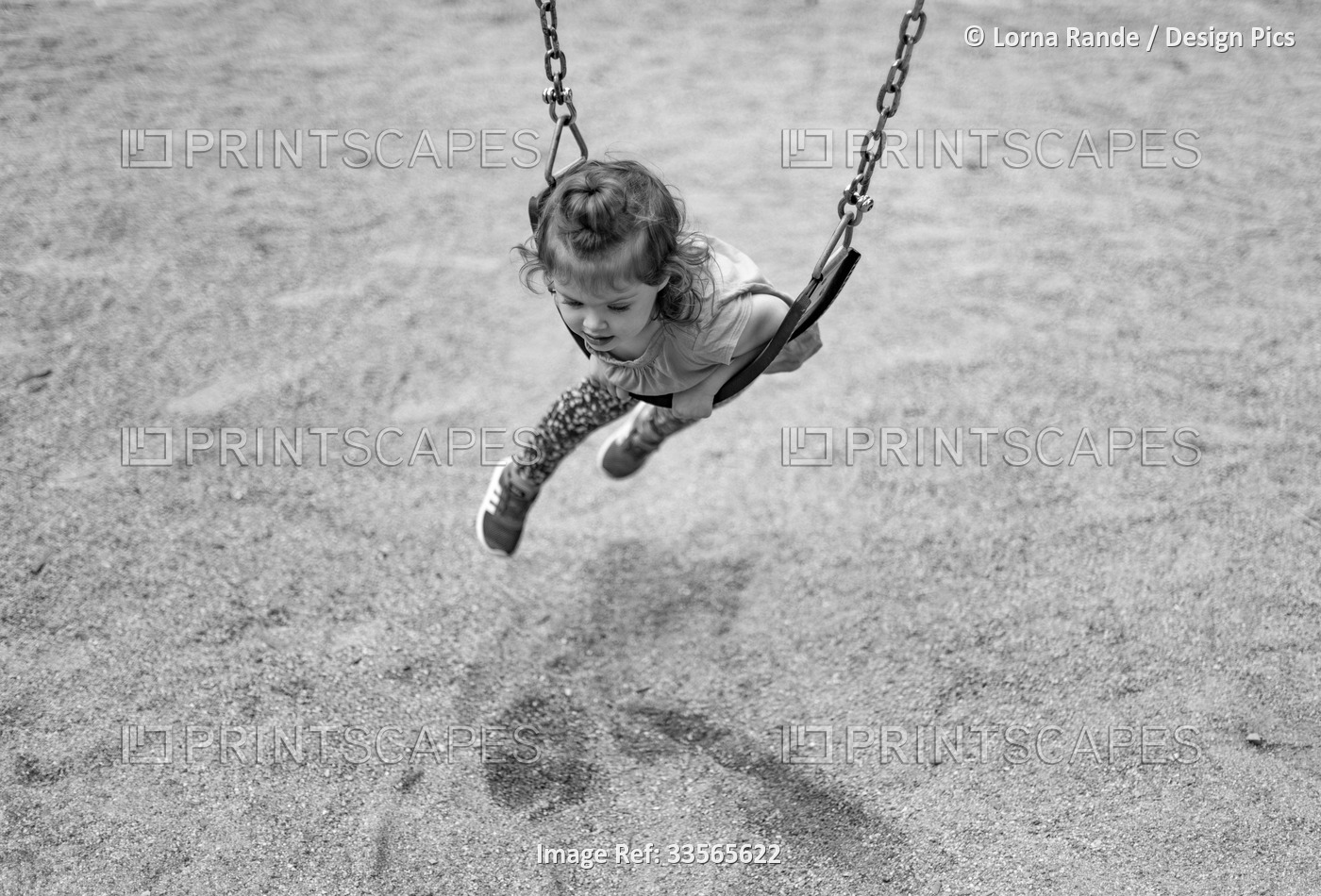 Black and white image of a preschooler girl laying across a swing on her belly ...