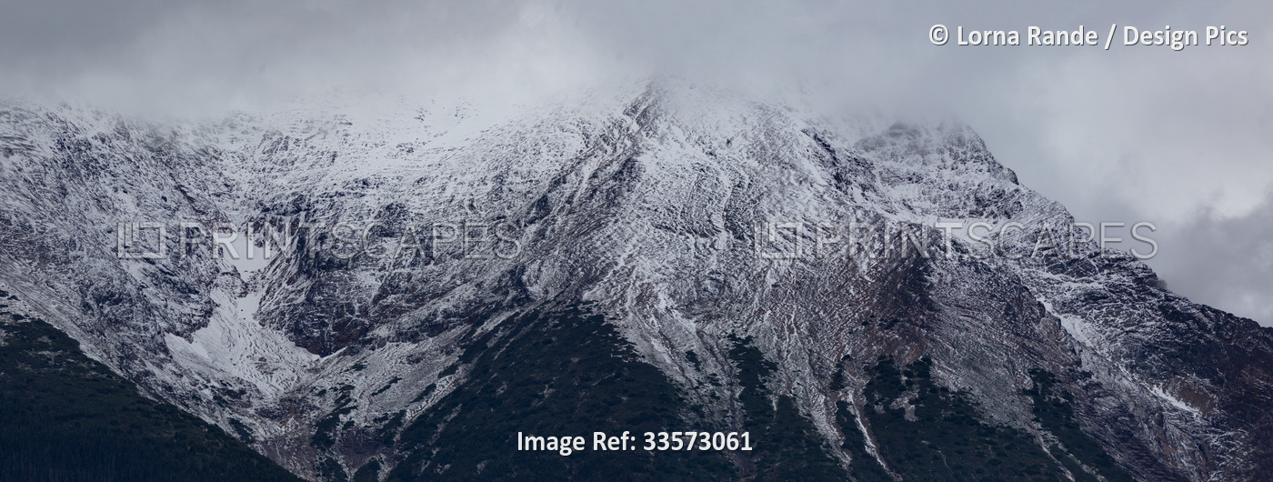 Black and white image of snow-capped mountaintops shrouded in clouds; British ...