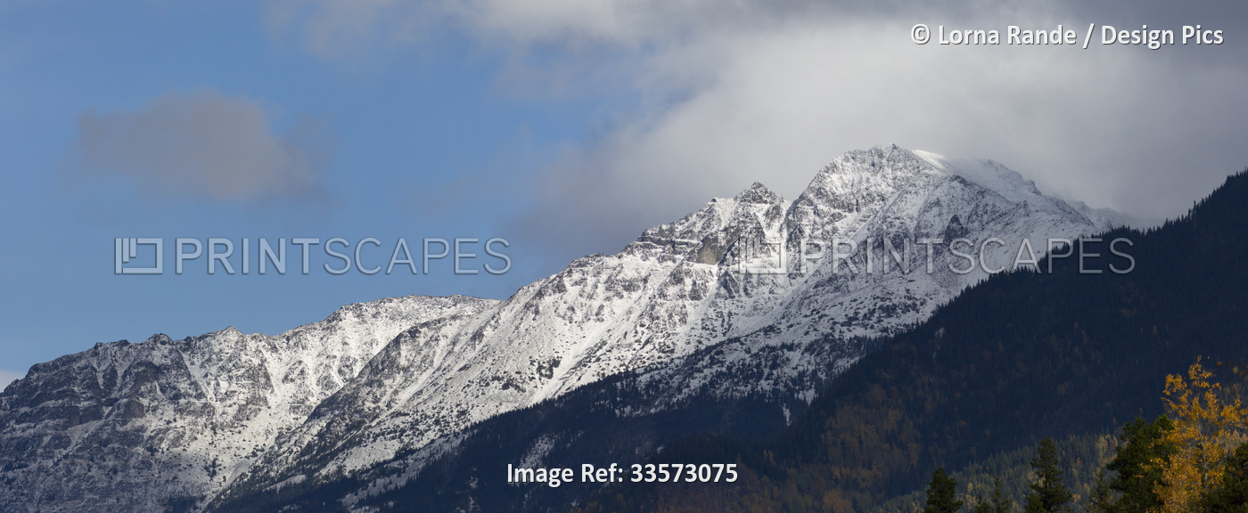 Snow-covered rugged mountaintops under a blue sky with clouds; British ...