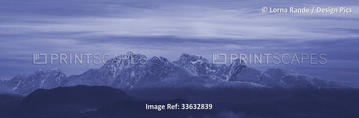 Rugged peaks of the Coast Mountains dusted with snow under a cloudy sky; ...