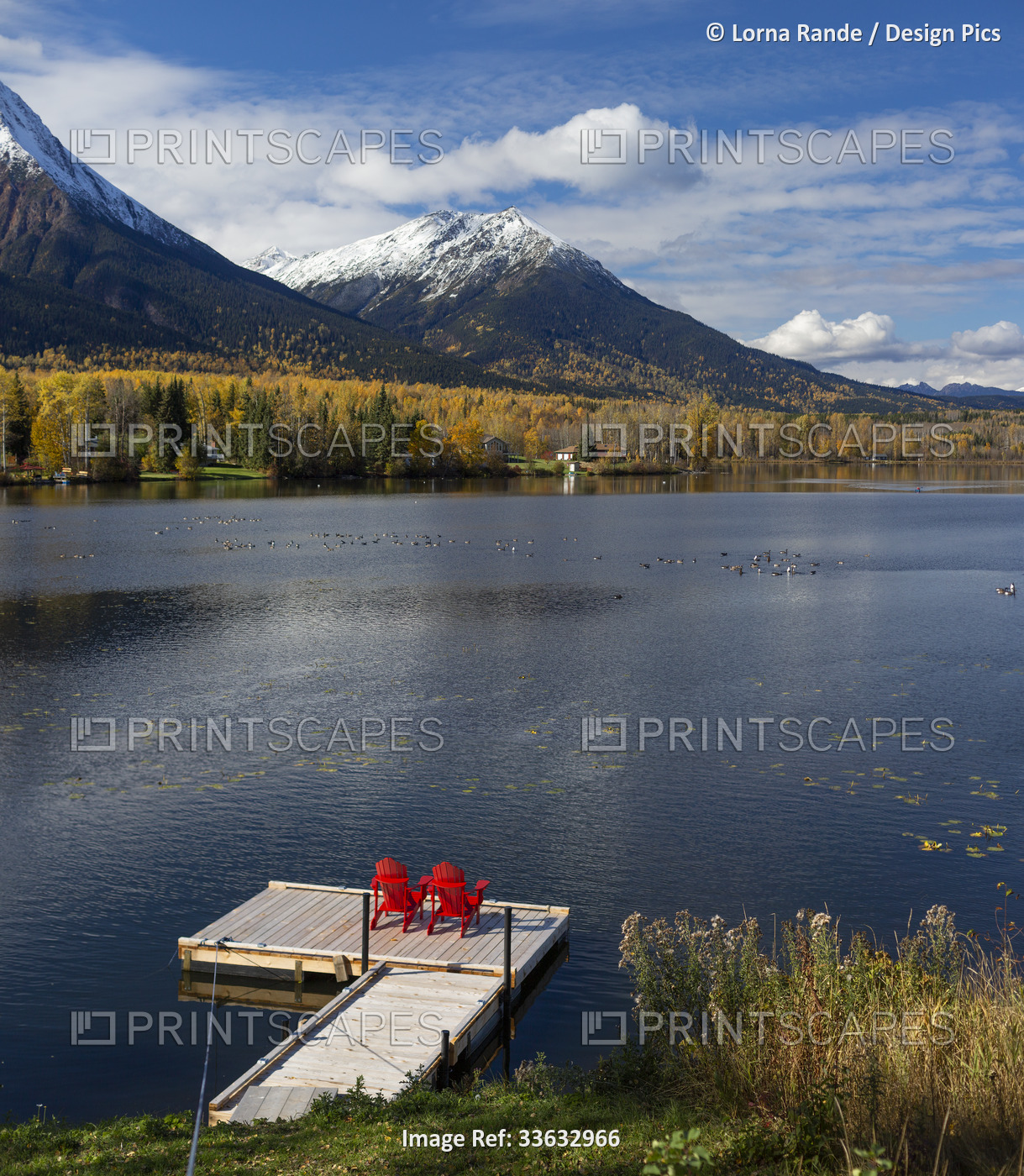 Two red chairs on a deck on tranquil Lake Kathlyn surrounded by autumn coloured ...