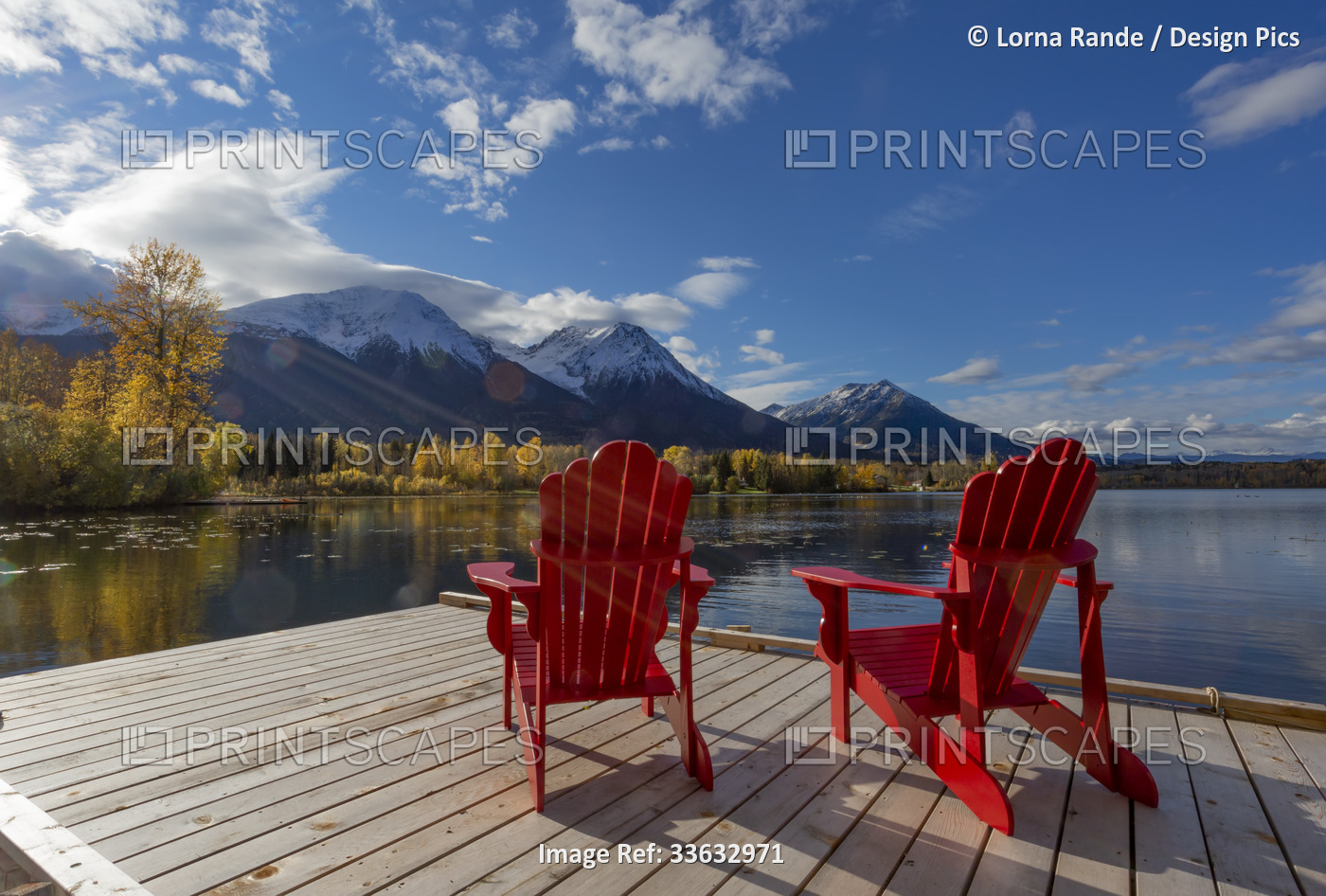 Two red chairs on a deck on tranquil Lake Kathlyn surrounded by autumn coloured ...