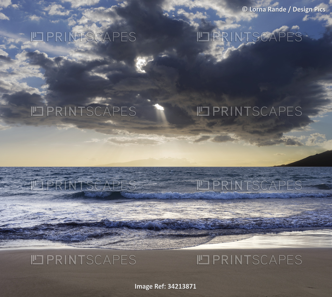 Breaking surf along the shoreline of Kamaole 2 Beach at twilight with sunrays ...