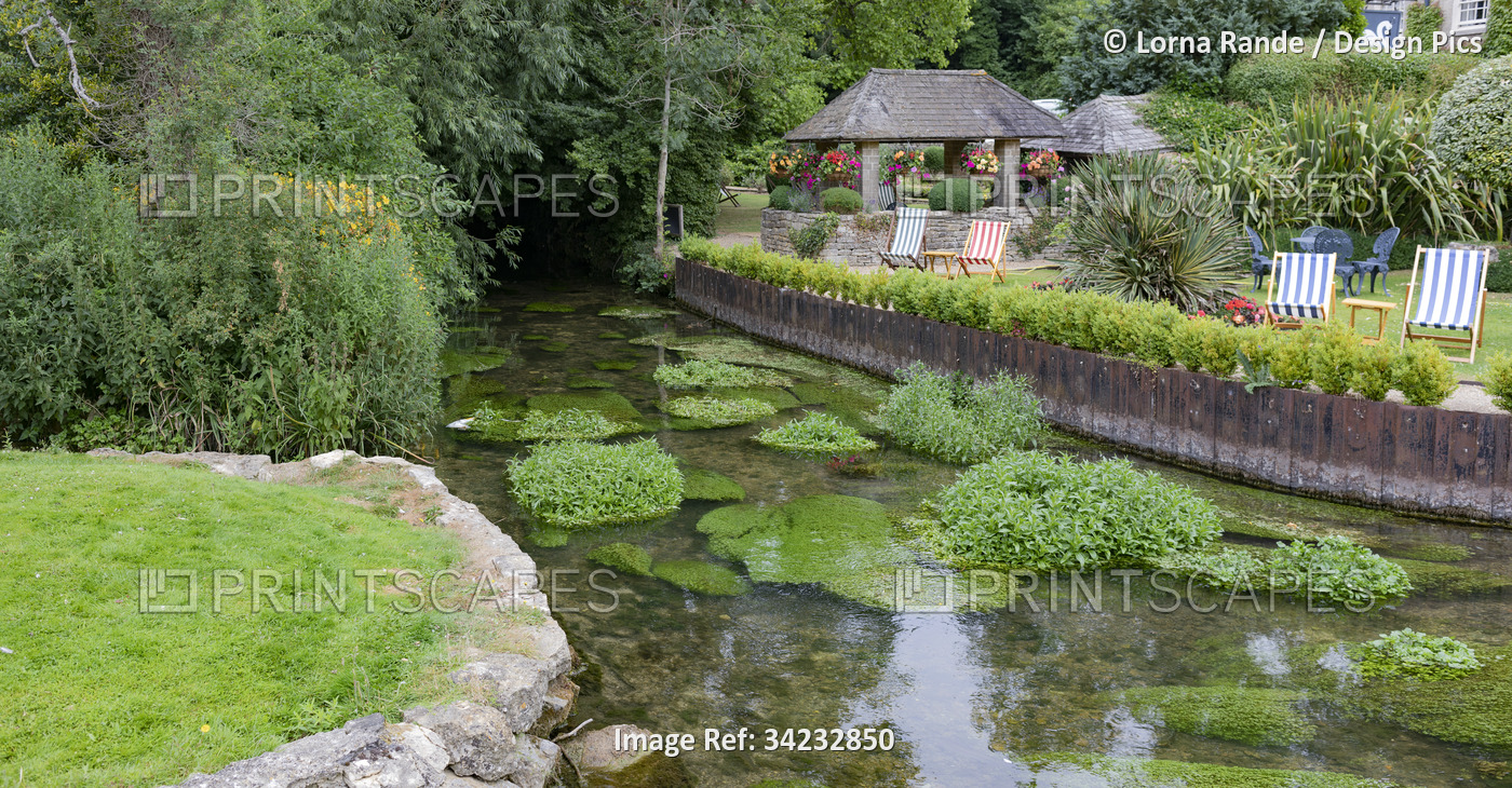 Riverside seating in gardens along the River Coln; Bibury, Gloucestershire, ...