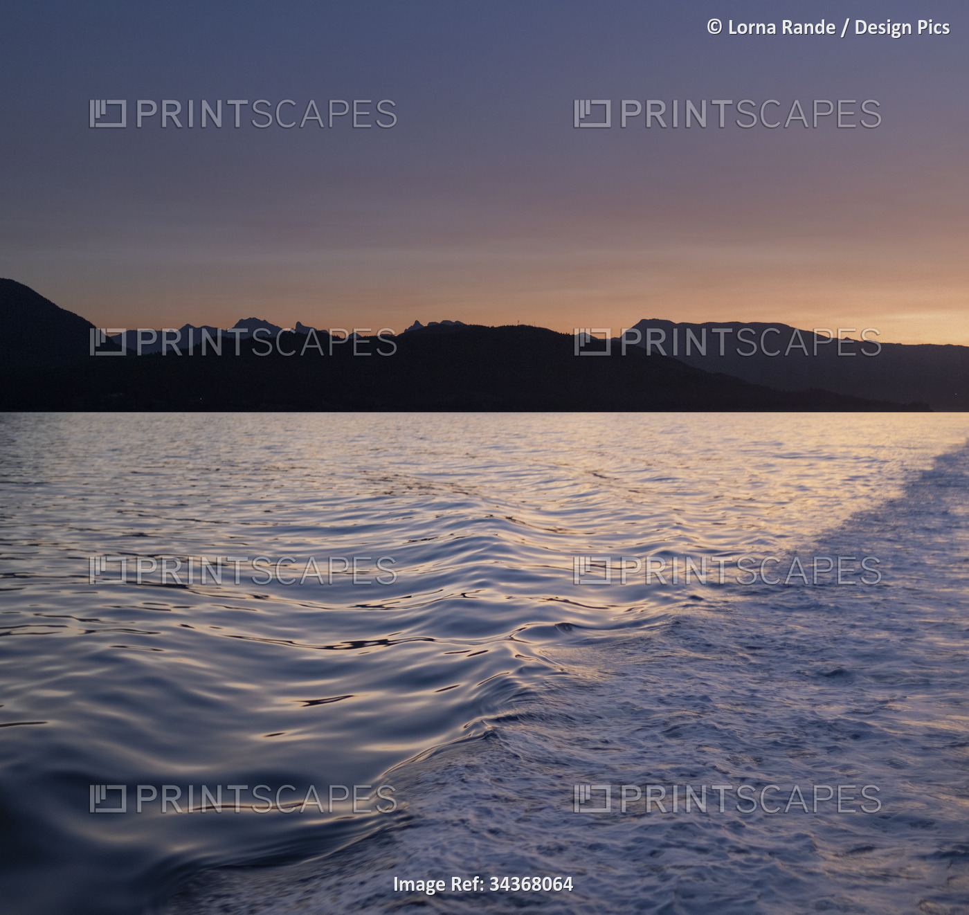 Ocean water swells in a boat wake at dawn with silhouetted mountains; British ...