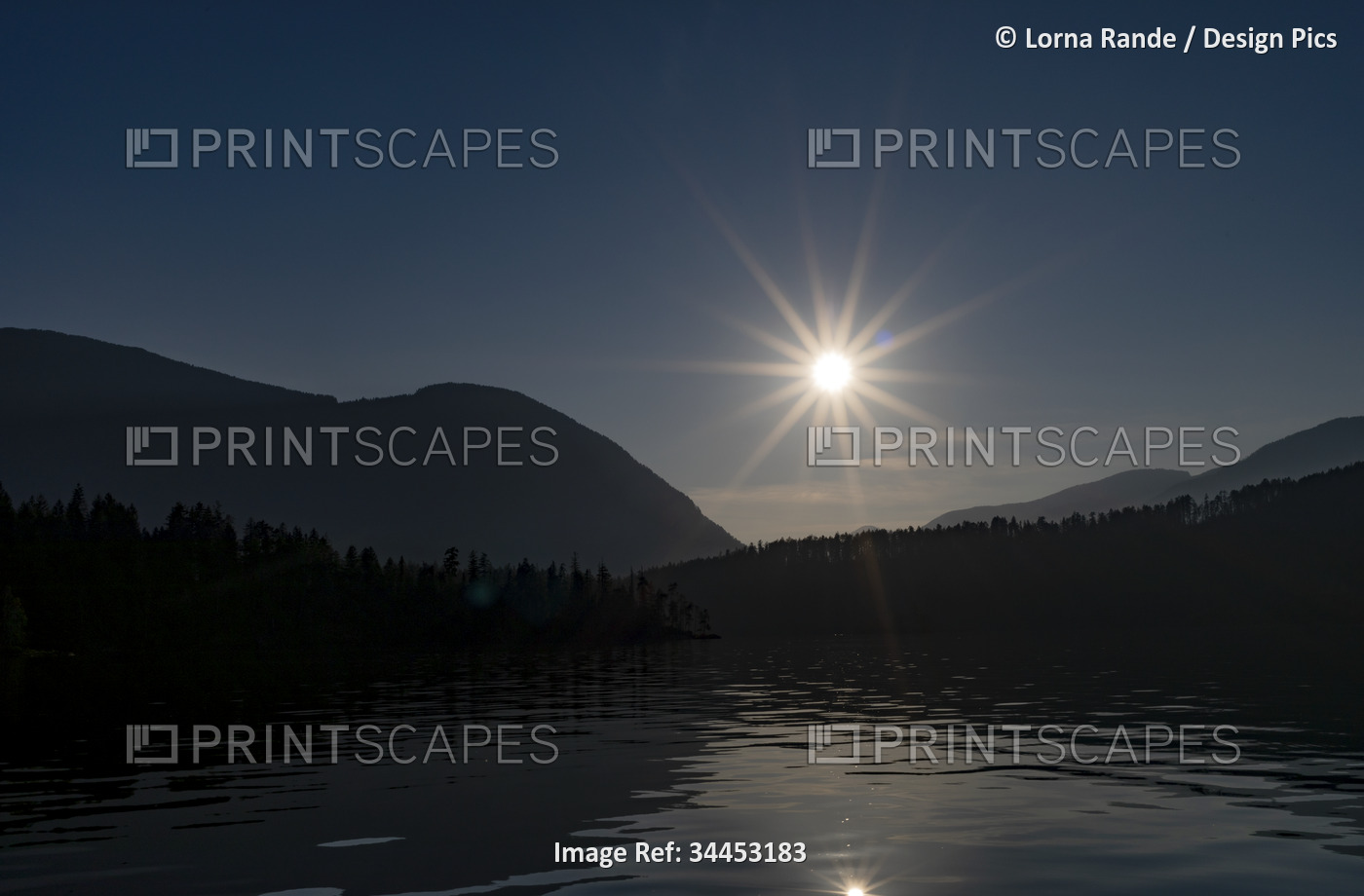 Sunburst over Sproat Lake with silhouetted Coast Mountains, Vancouver Island, ...