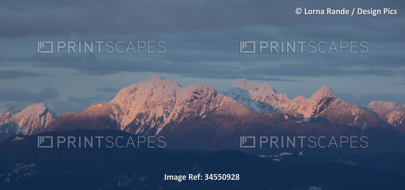 Snow-capped mountain range illuminated with soft light under a blue sky with ...